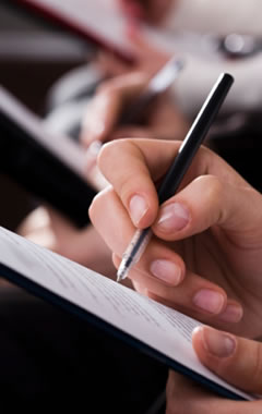 close up image of office workers taking notes focusing on an individuals hand with pen to notebook